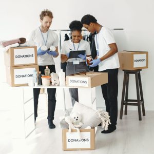 Three volunteers organize donation boxes filled with essentials in a bright indoor setting.
